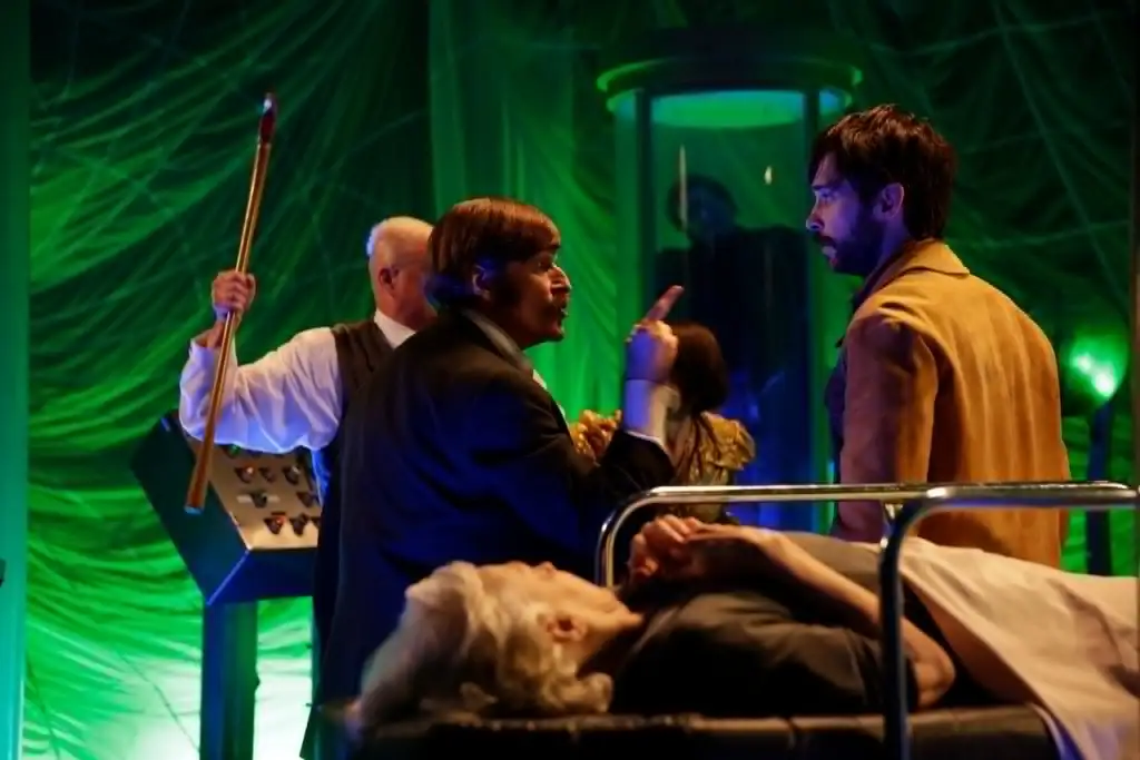 A woman lying on a hospital bed with medical staff and visitors around, in a green-lit sci-fi settin.