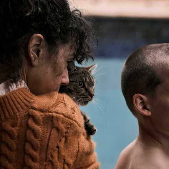 Abandoned woman holding cat with a young boy with scars on face, emotional scene from The Scariest Things.