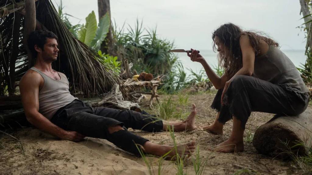 A woman pointing a gun at a man lying on the ground in a jungle setting.