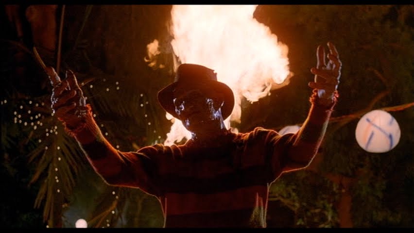 A fiery performer with hands raised during a horror-themed fire show.
