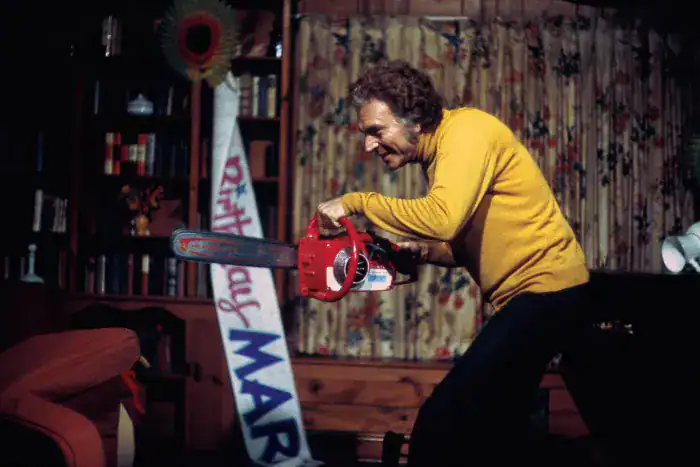A chainsaw-wielding maniac in a yellow sweater attacking a person in a horror scene.
