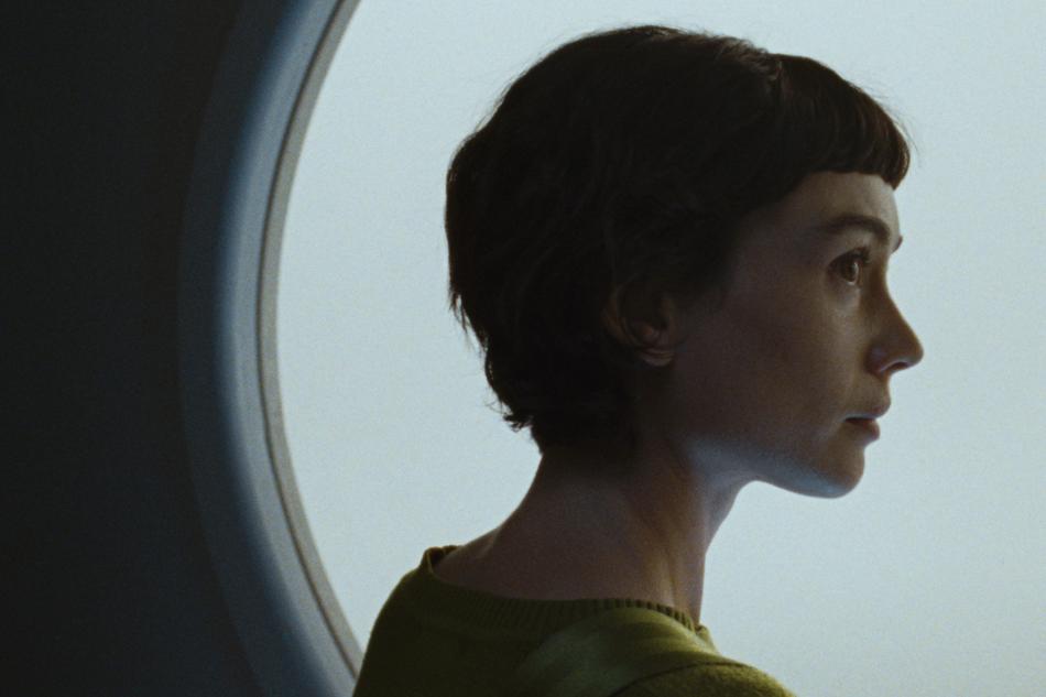 A woman looking out of a circular window, contemplating, with a serious expression.