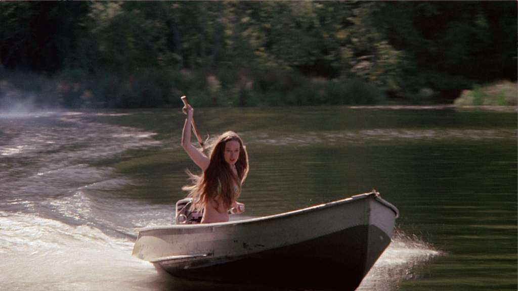 A woman in a boat on a river during daytime, with trees in the background.