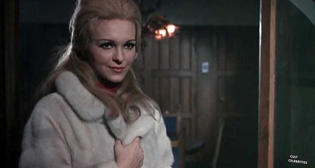 A woman with blonde hair in a cozy coat inside a rustic wooden cabin.