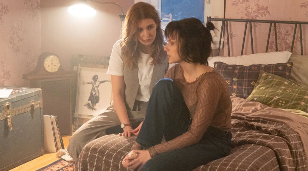 A haunting scene from the movie Whistle (2025) featuring two women in a dimly lit bedroom.