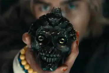 A menacing black skull mask with glowing eyes held up by a person in a dark setting.