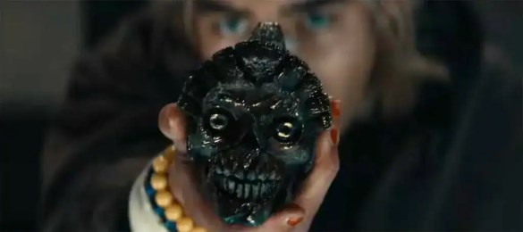 A menacing black skull mask with glowing eyes held up by a person in a dark setting.