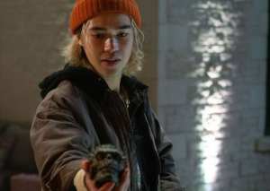 Young woman in a beanie holding a small creature, urban background, moody lighting.