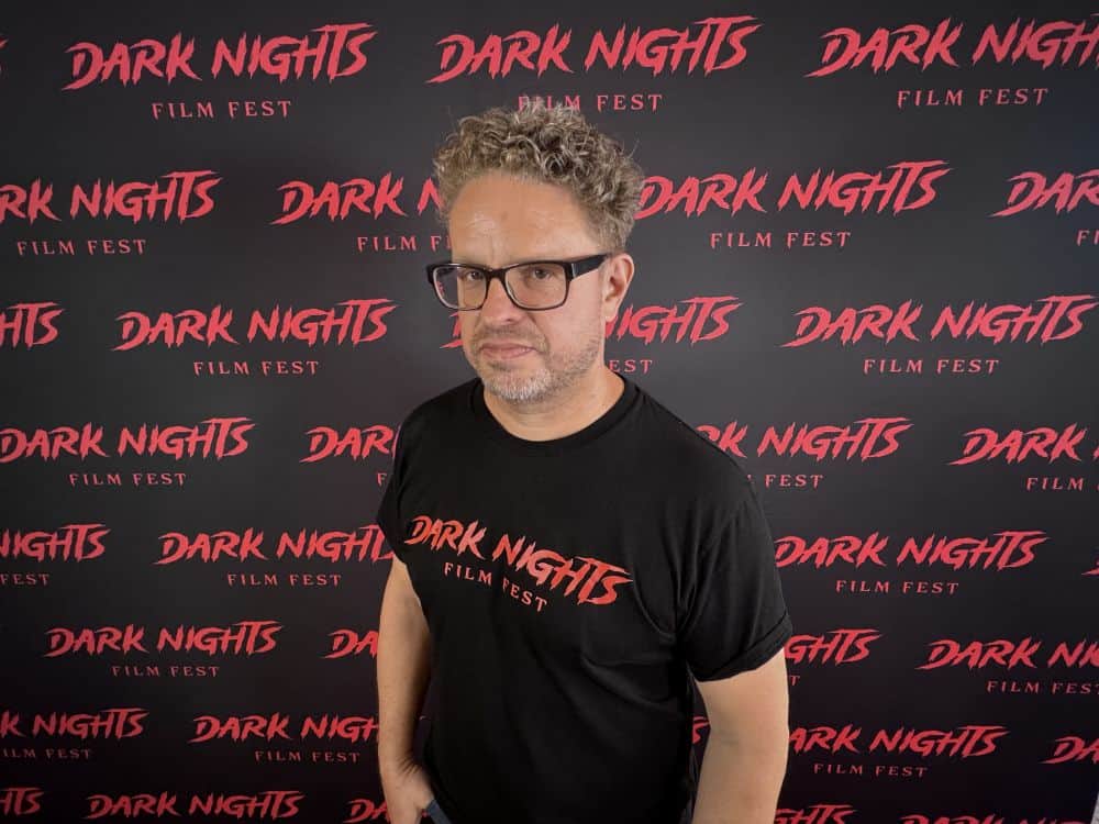 Haunted movie festival attendee wearing a black "Dark Nights" T-shirt at Dark Nights Film Fest backd.