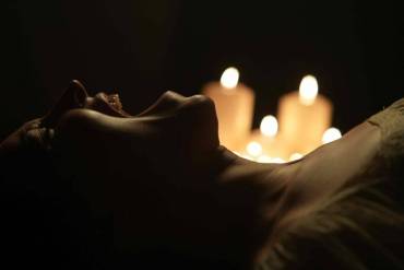 A woman lying in darkness with candles creating a spooky, eerie atmosphere.