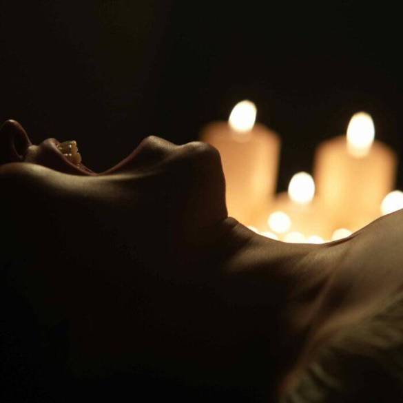 A woman lying in darkness with candles creating a spooky, eerie atmosphere.
