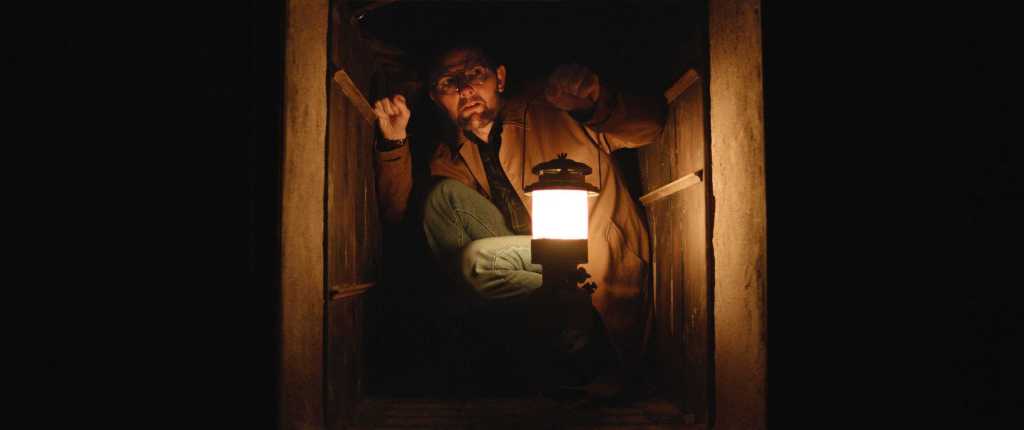 A man with a lantern peering out from a dark, narrow space at night.
