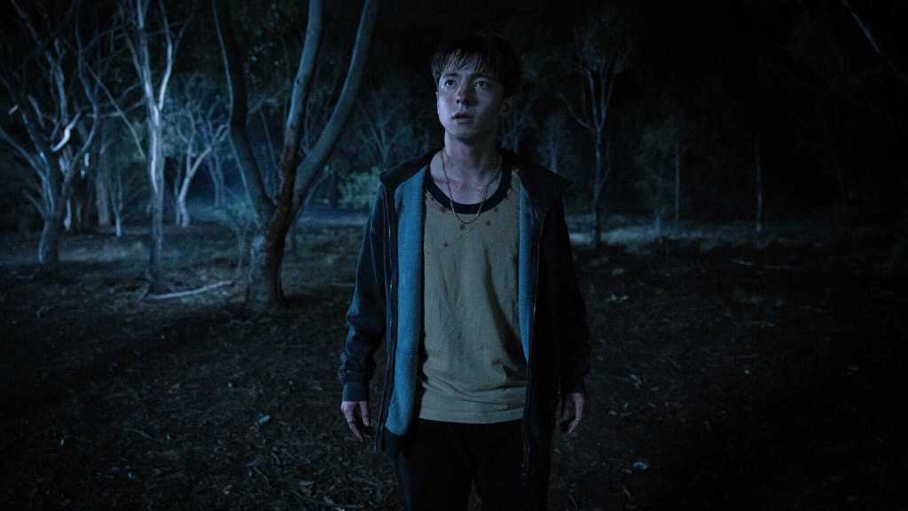 A dark, eerie forest scene with a young boy standing alone under moonlight, creating a spooky atmosp.