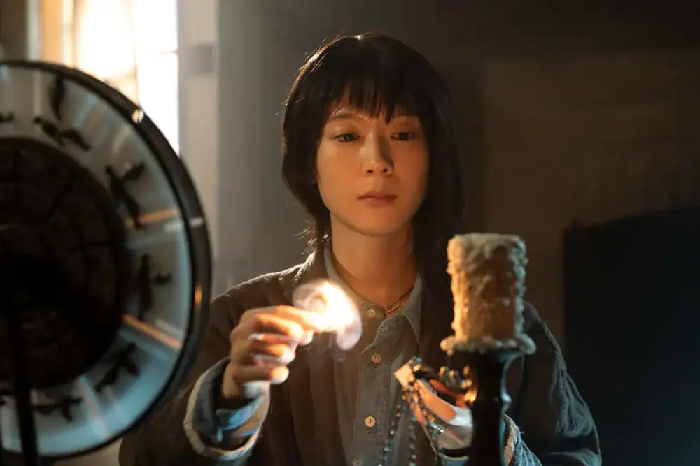 A woman examining a mysterious device with a glowing light in a dimly lit room.