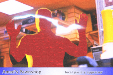 A man in a red shirt with hands raised inside a pawnshop.