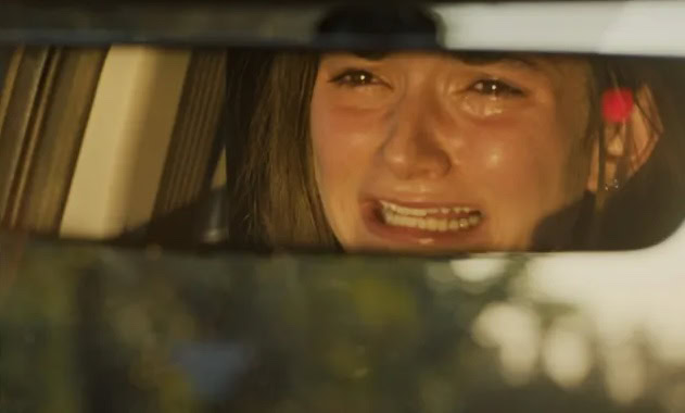 A woman with a distressed expression looking through a car rearview mirror.