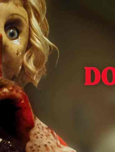 Eerie doll with cracked face and glowing eye, holding finger to lips in a spooky pose.