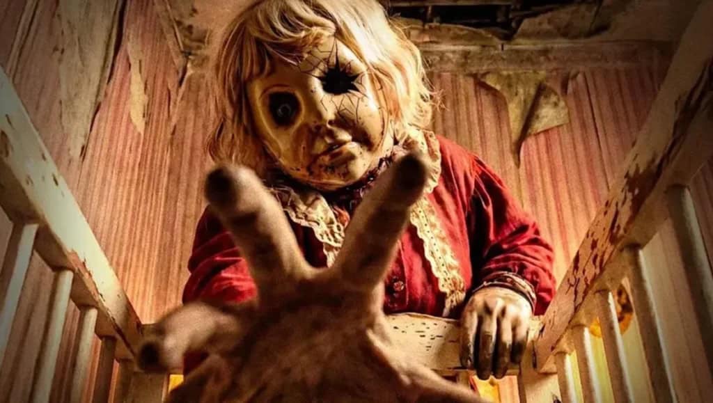 A terrifying doll with a cracked face and one eye missing, reaching out menacingly.