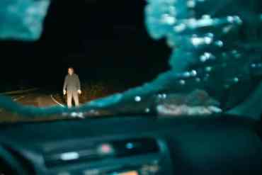 A haunting figure standing in the middle of a dark, deserted road at night.