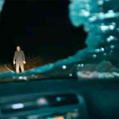 A haunting figure standing in the middle of a dark, deserted road at night.