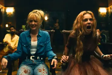 A woman with long blonde hair screams in terror during a tense scene in a dimly lit room.