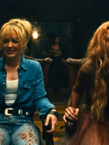 A woman with long blonde hair screams in terror during a tense scene in a dimly lit room.