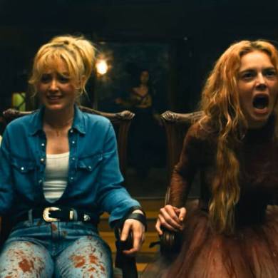 A woman with long blonde hair screams in terror during a tense scene in a dimly lit room.
