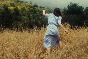 Haunted girl running through tall grass in a spooky outdoor setting.