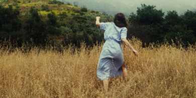 Haunted girl running through tall grass in a spooky outdoor setting.