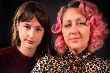 Two women with contrasting hair colors posing together against a dark background.