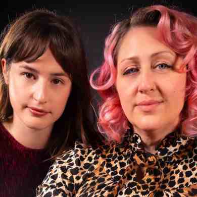 Two women with contrasting hair colors posing together against a dark background.