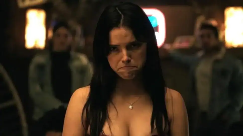 A woman with long dark hair looking upset in a dimly lit room.