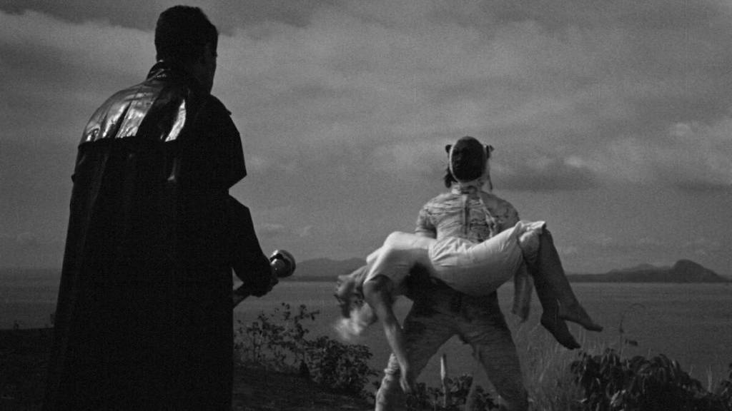 A man holding a woman in his arms by a lake at sunset, black and white image.