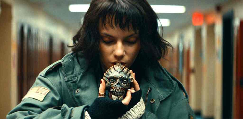 A woman holding a creepy skull mask in a school hallway.