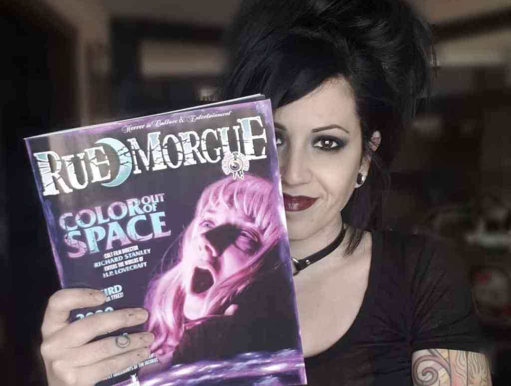Goth woman holding a Rue Morgue magazine with a spooky cover image.
