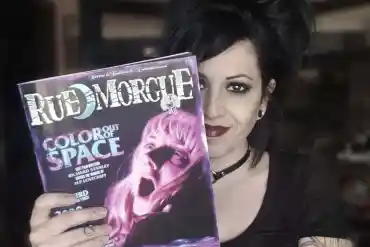 Goth woman holding a Rue Morgue magazine with a spooky cover image.