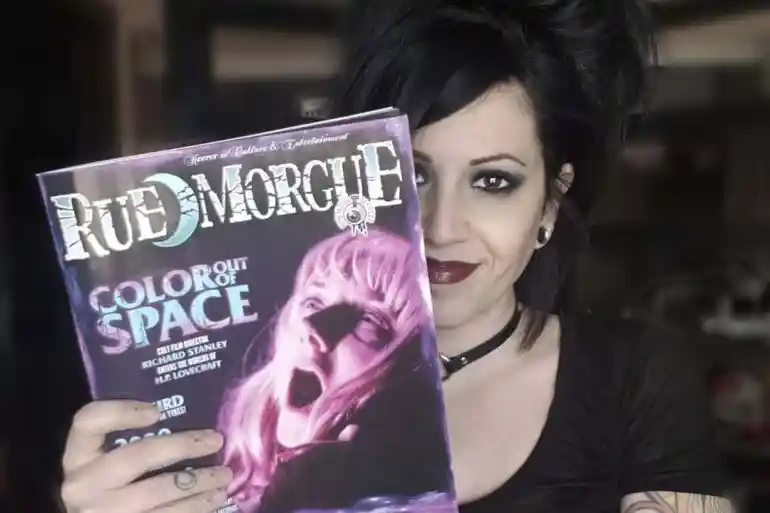 Goth woman holding a Rue Morgue magazine with a spooky cover image.
