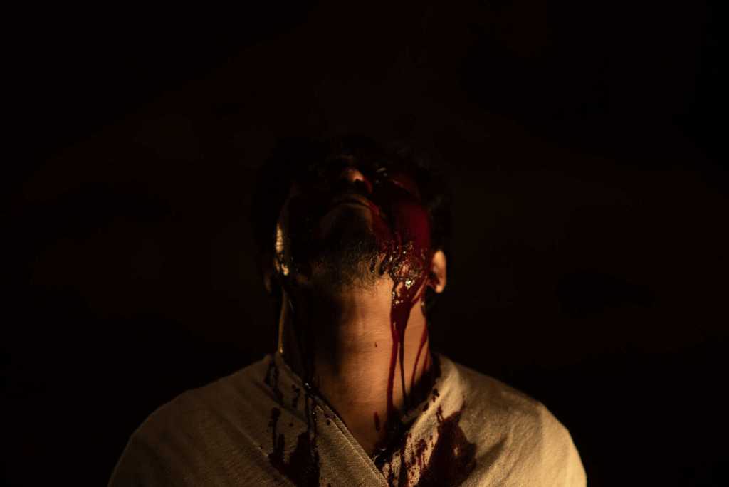Dark, eerie image of a person with blood on their face and neck in a horror setting.