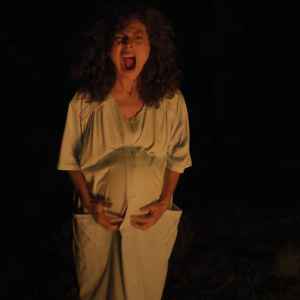 Woman with curly hair screaming in darkness, holding her stomach.