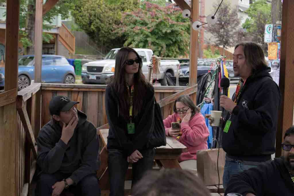 Group of people at outdoor event, one speaking into microphone, others listening.