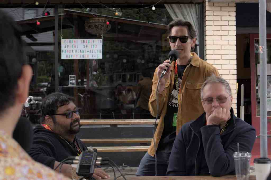 Man speaking into microphone at outdoor event with seated audience.