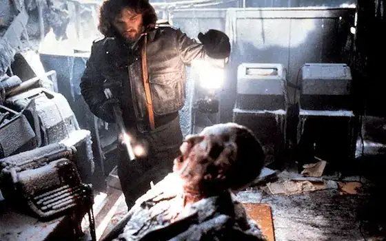 A man with a flashlight investigates a gruesome, frozen corpse in a dark, icy room.