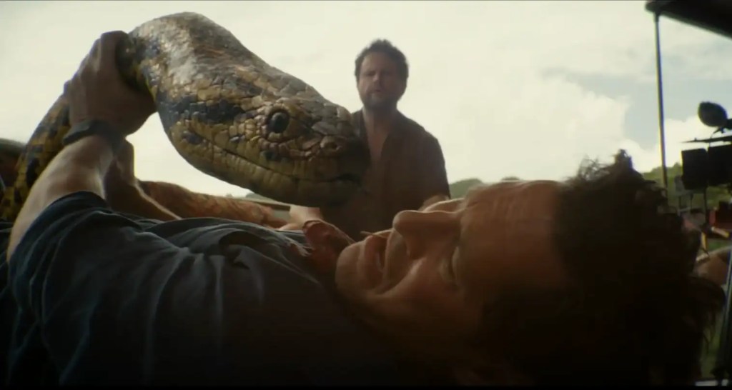 A man is attacked by a large snake in a tense scene from Anaconda (2025) review.