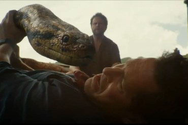 A man is attacked by a large snake in a tense scene from Anaconda (2025) review.