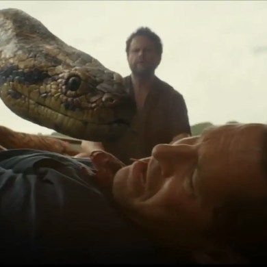 A man is attacked by a large snake in a tense scene from Anaconda (2025) review.