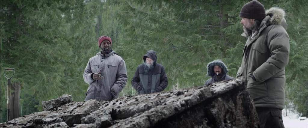 Group of people in winter clothing exploring a forested area with a large fallen log.