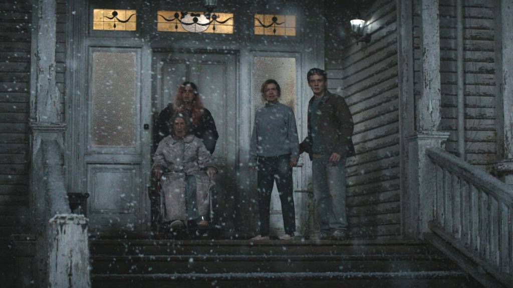 Group of four people standing on porch in snow at night, eerie scene from horror film.