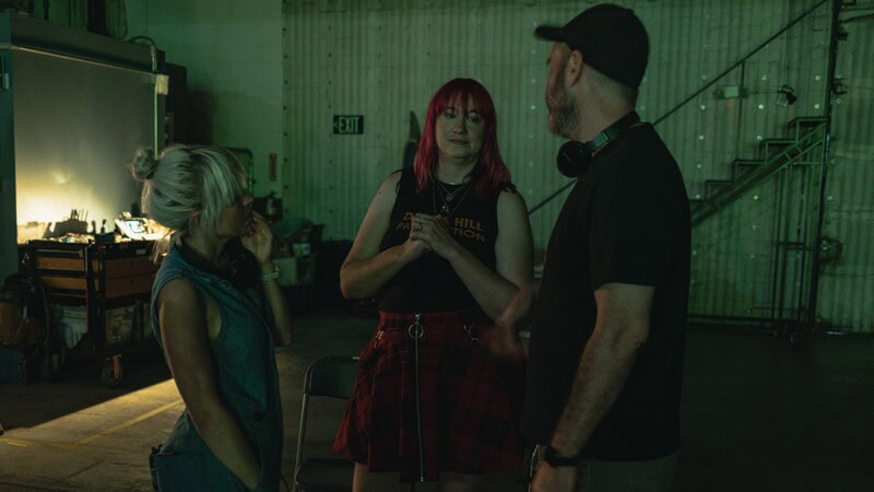 Three people in conversation at a dimly lit event space with green lighting.