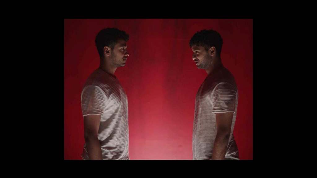 Two young men face each other against a red background, mirror images.
