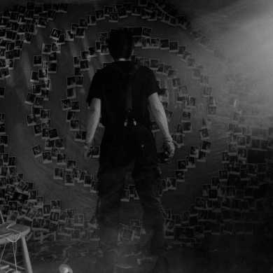 Person standing in front of a spiral of Polaroid photos on a wall.
